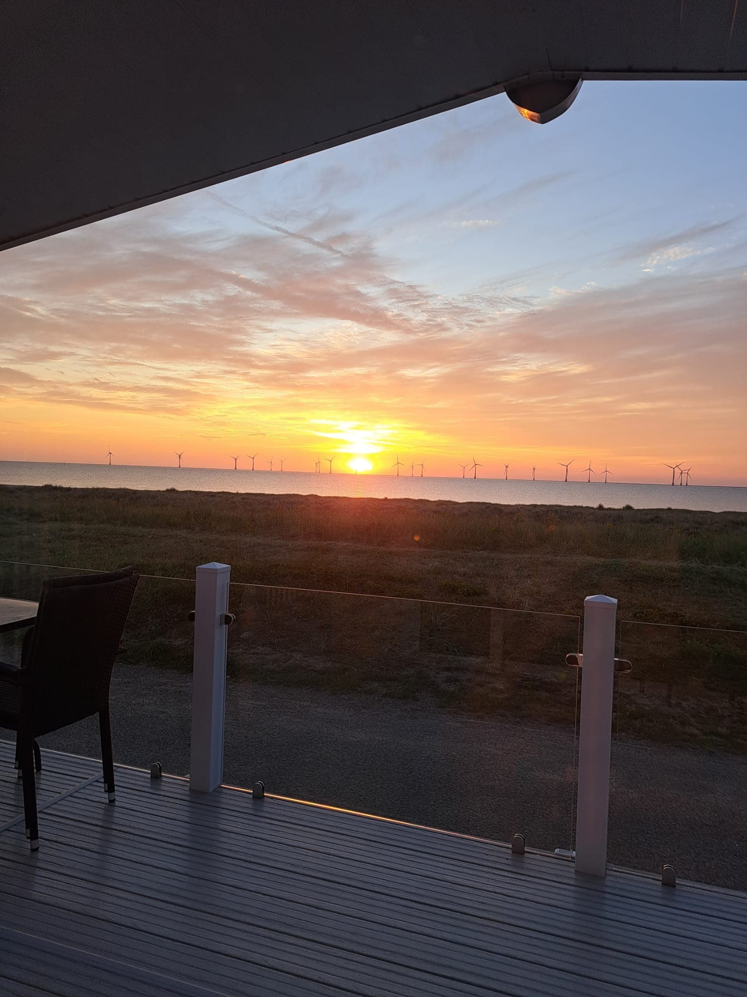 Sunset over the sea and wind farm, viewed from the caravan's private decking